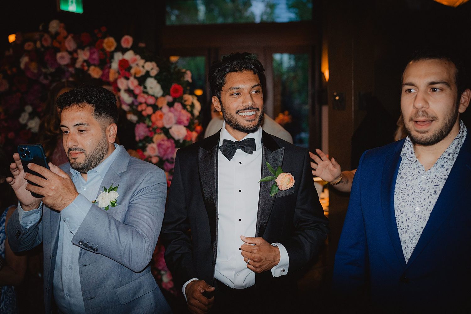 Wedding reception guests in formal attire mingle and socialize under ambient lighting.