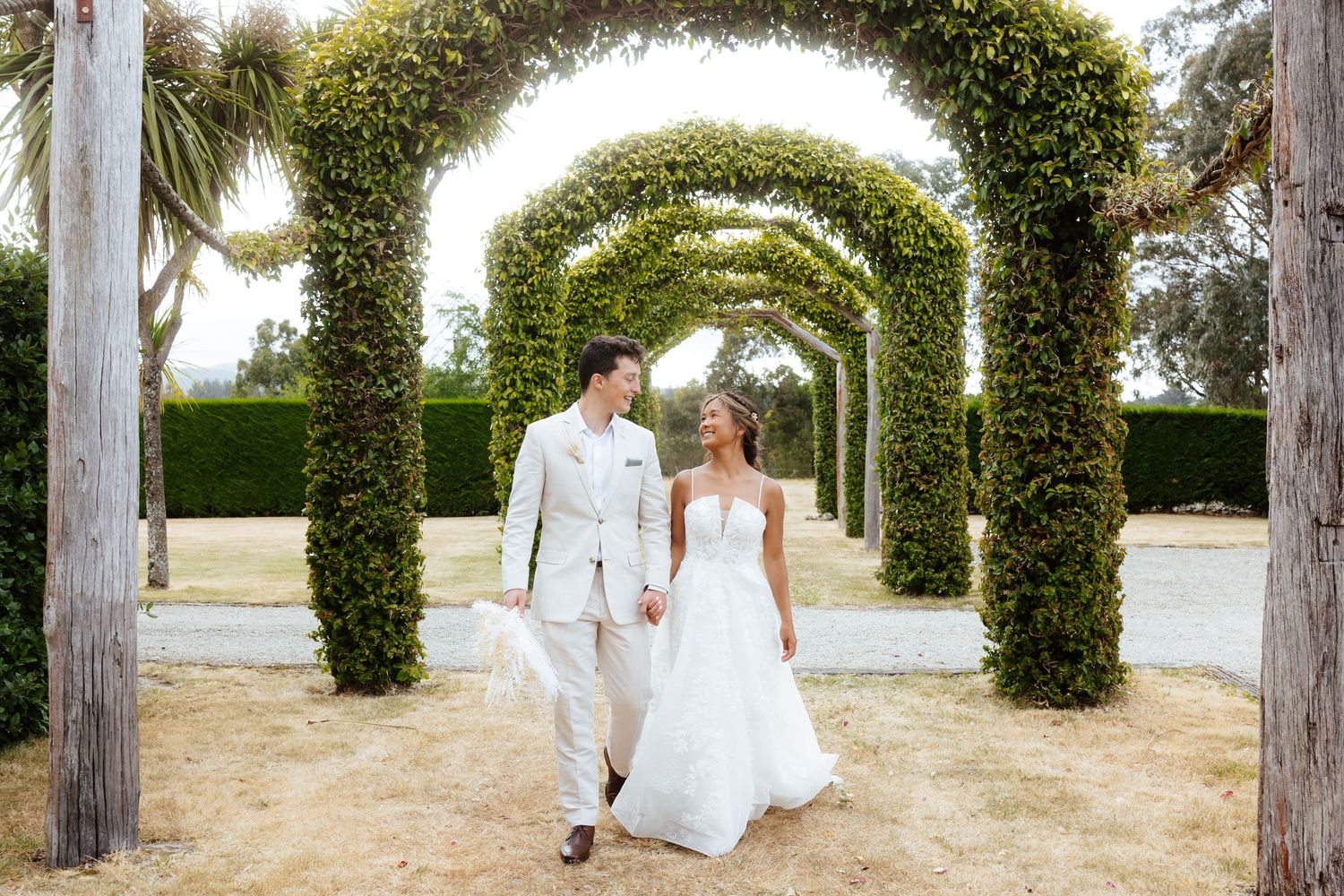 Wedding ceremony guests toss confetti over couple walking down garden path.