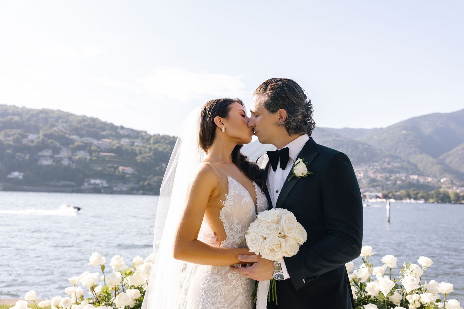 A romantic wedding couple shares intimate moments against a scenic coastal backdrop with mountains and water views.