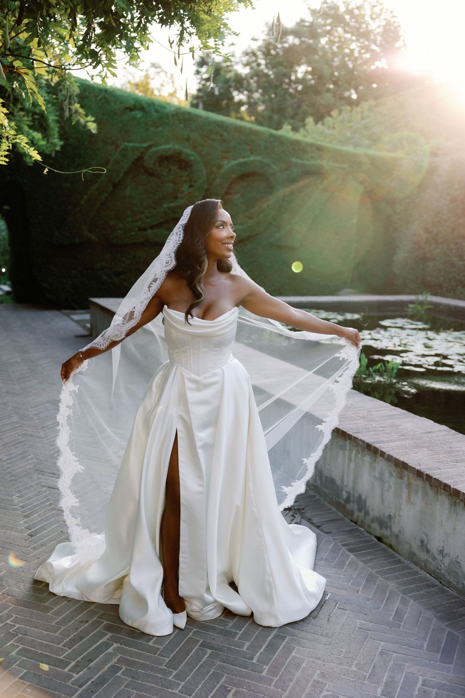 A person in a flowing white gown poses gracefully on brick pavement during a golden sunset photoshoot.