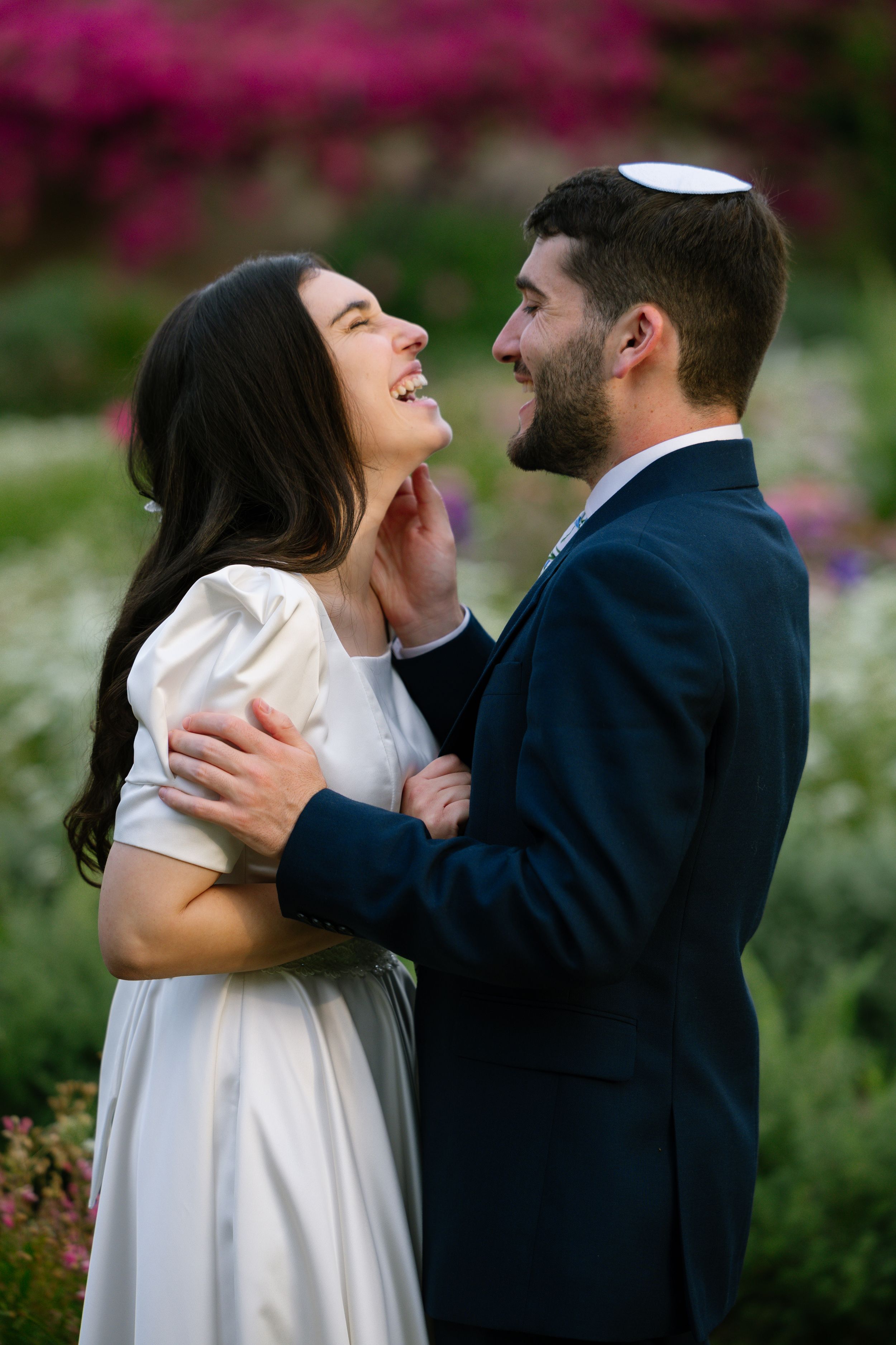 A couple shares a joyful moment together in a garden with vibrant pink flowers in the background.