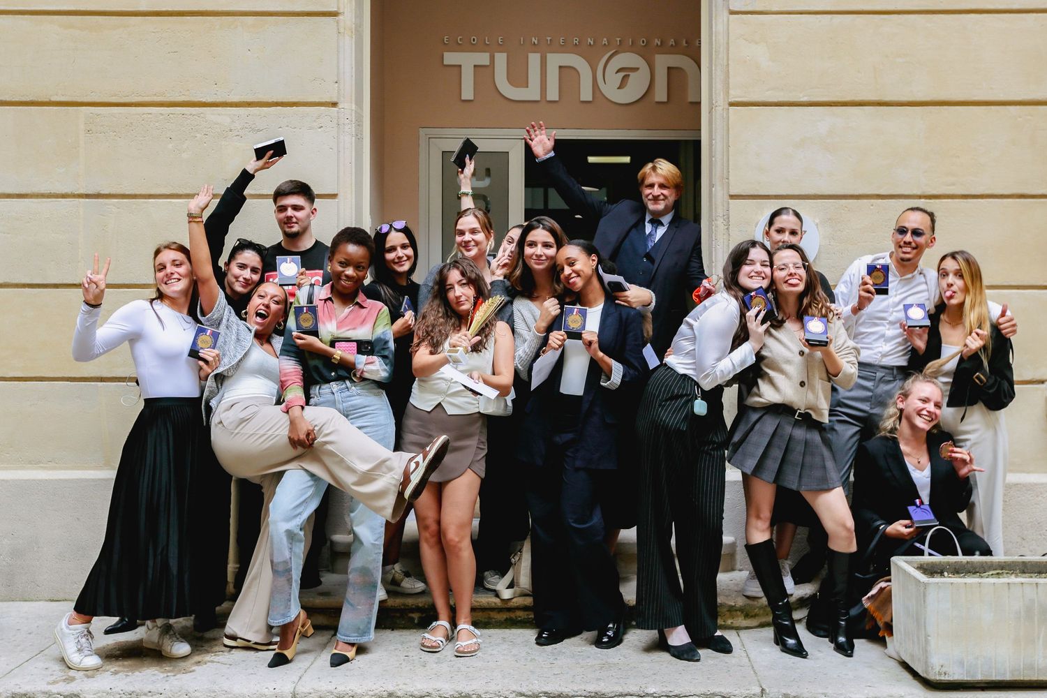 Excited group of students celebrating and posing energetically outside the Tunon school entrance.