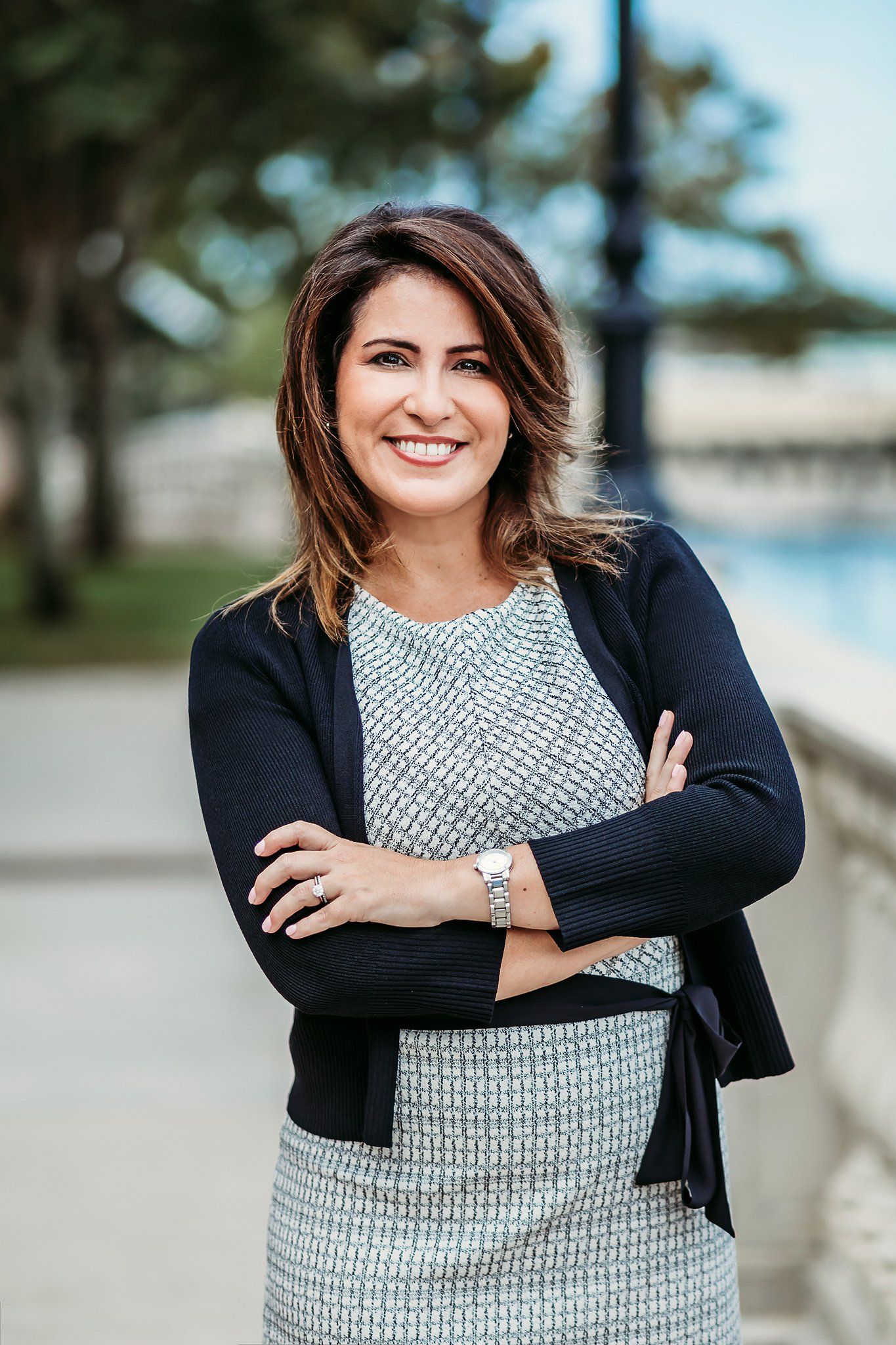 Professional portrait of someone wearing a gray knit dress and black cardigan standing outdoors near water.