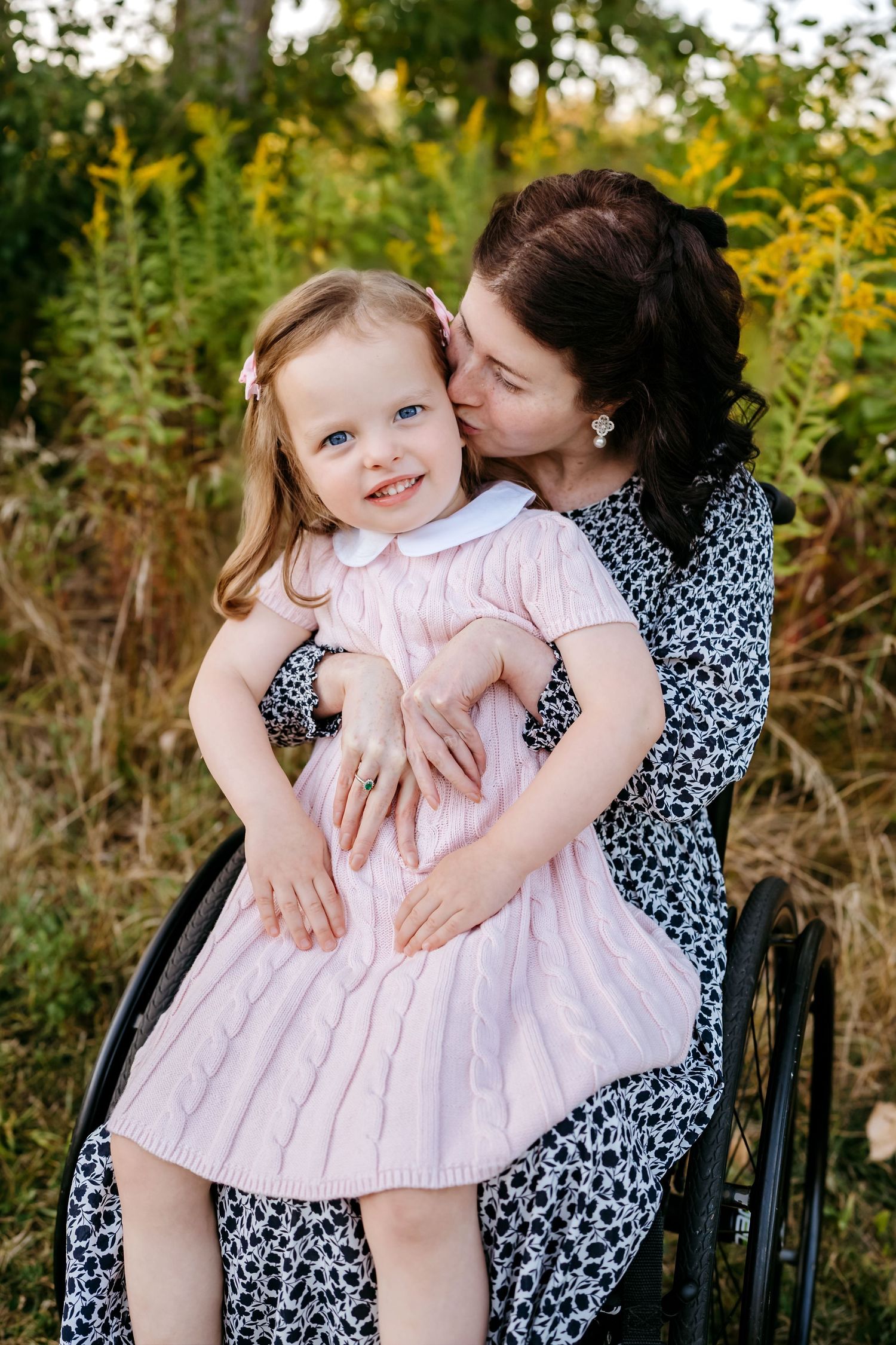 A sweet outdoor family photoshoot in a garden with a pink dress and floral print dress against natural foliage.