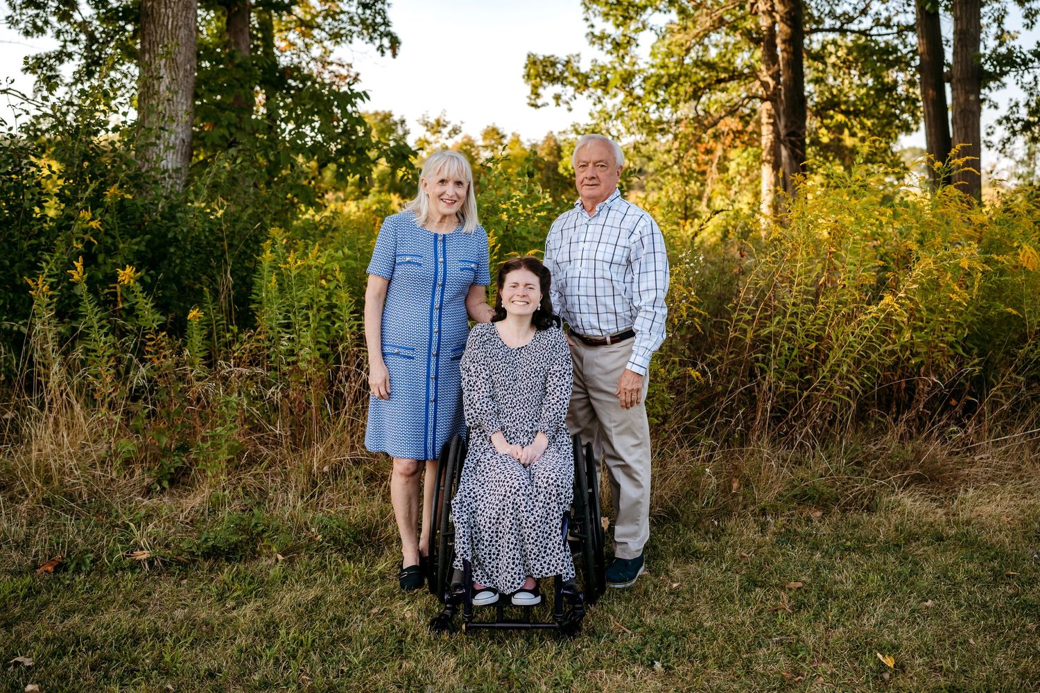 Family portrait session in a golden autumn field at sunset with trees in the background.