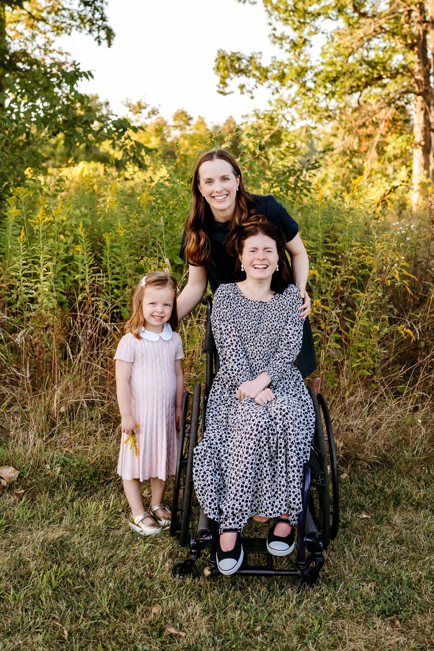 An inclusive family photoshoot in a meadow at golden hour featuring a wheelchair and pink dress.