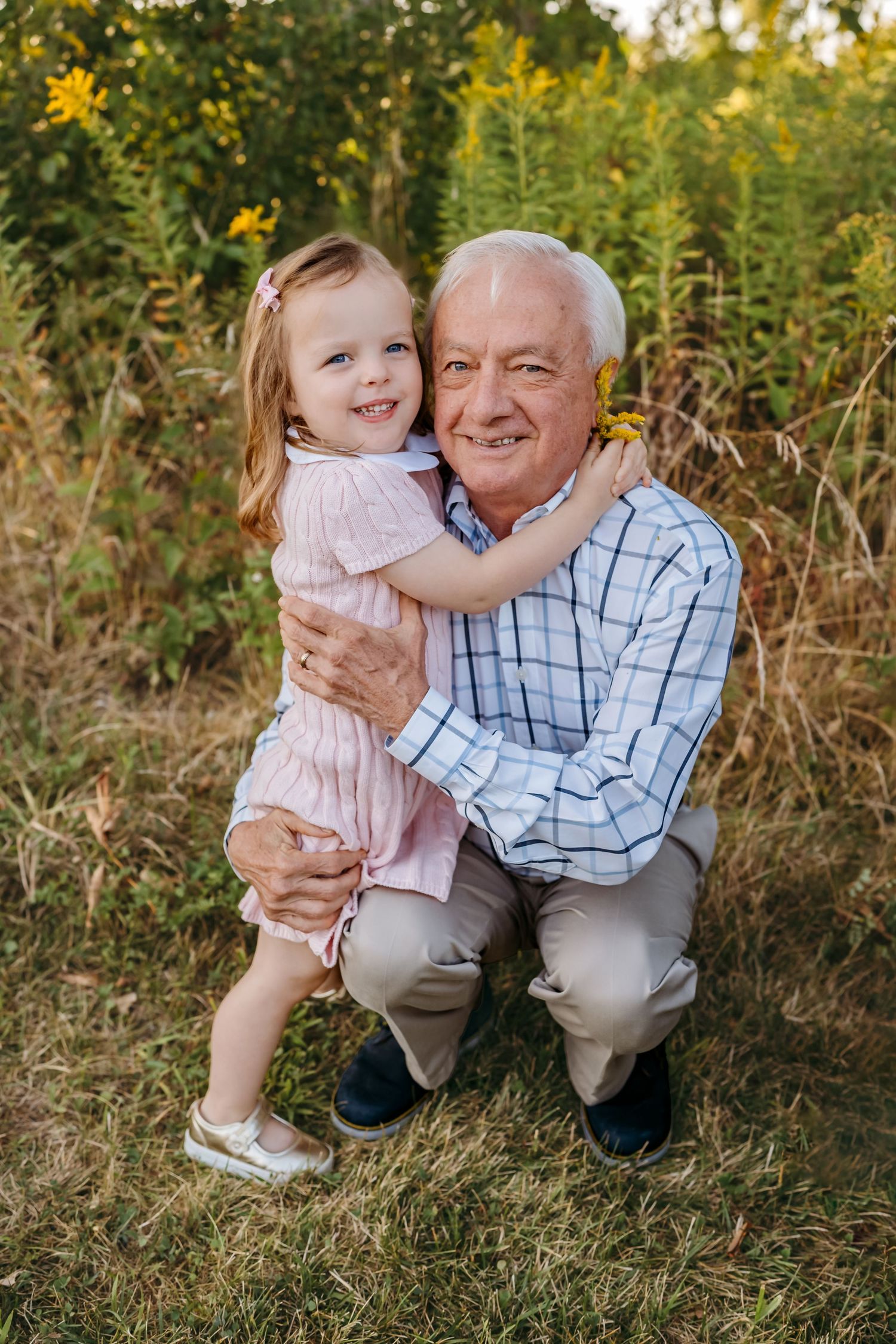 A tender outdoor family moment captured in a field of tall grass and wildflowers during golden hour.