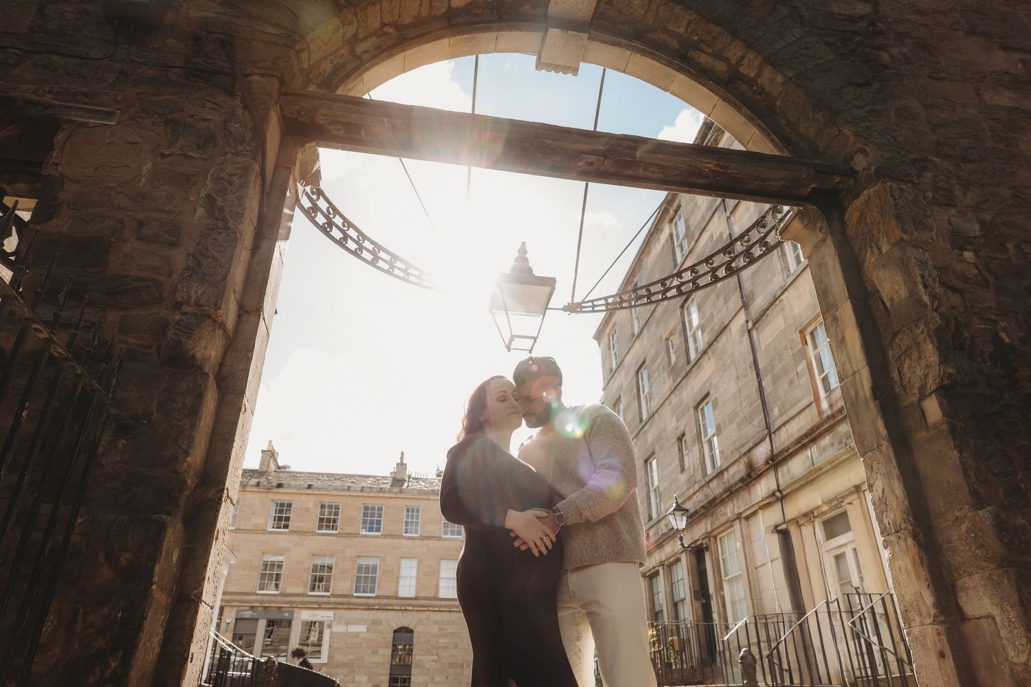 A couple shares a romantic moment under an ornate stone archway in Bath's historic Royal Crescent.