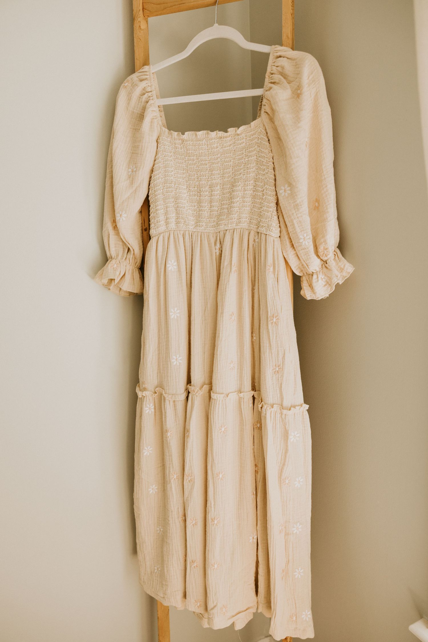 Delicate white lace baby romper with ruffled trim and peach bow detail laid on brown fabric.
