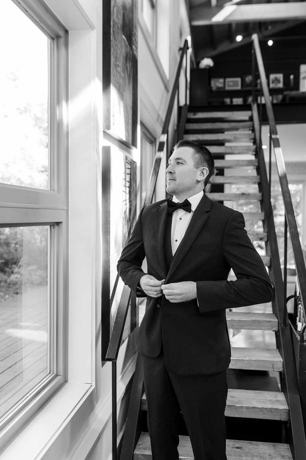 A person in a black tuxedo stands by a window in a formal setting, creating an elegant silhouette effect.
