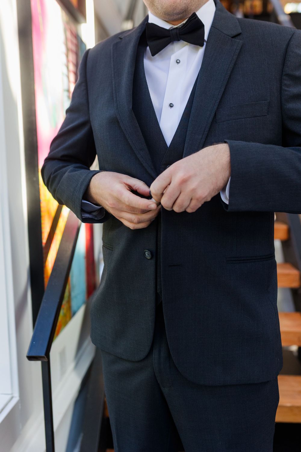 Man in black tuxedo adjusts his suit jacket while getting ready for formal event.