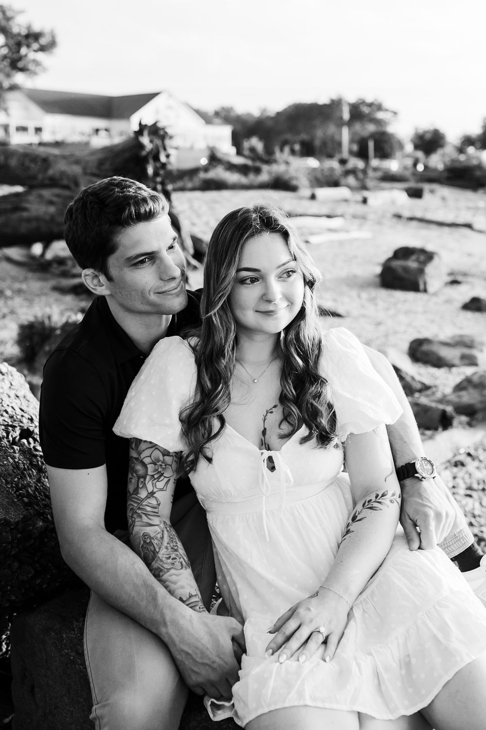 A couple shares intimate black and white moments on a rocky shoreline.