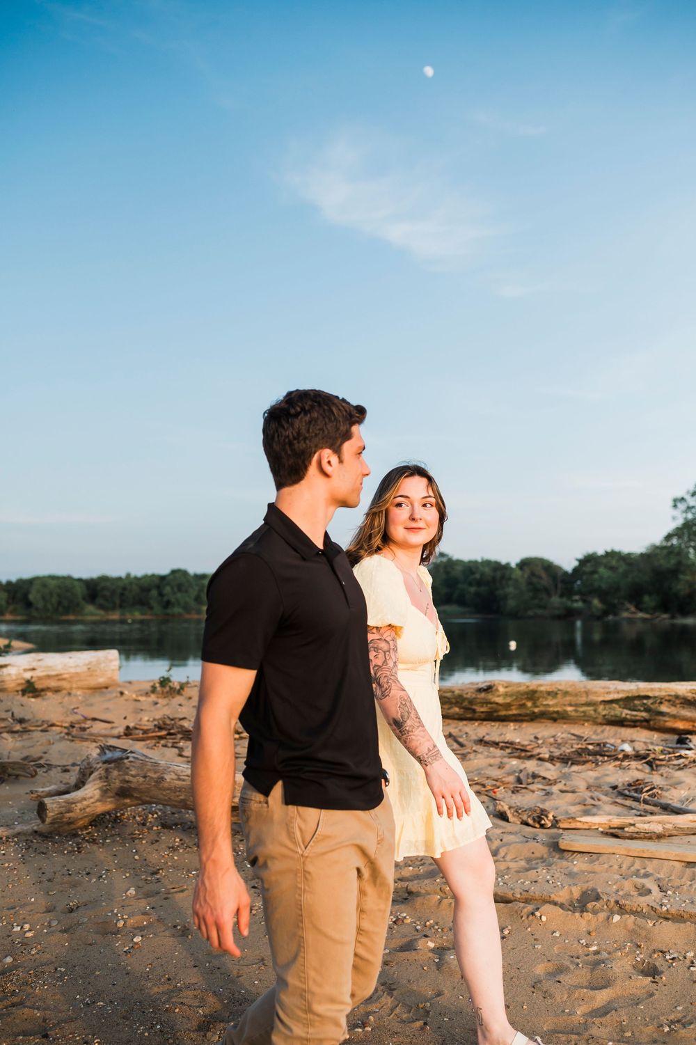 A couple in casual attire poses together on a rocky beach landscape during sunset.