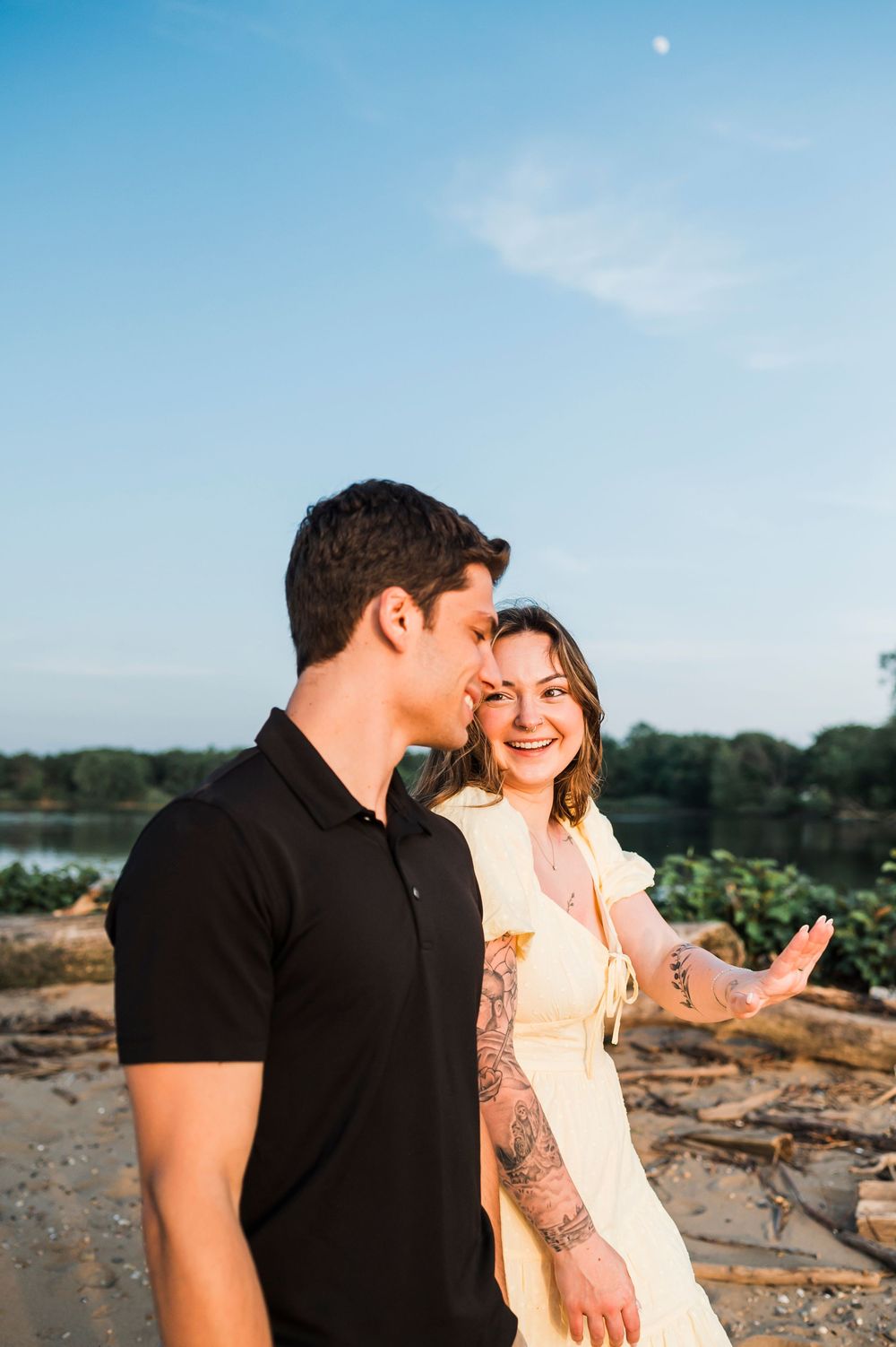 Two people share an intimate moment on a beach path at sunset with blue skies overhead.