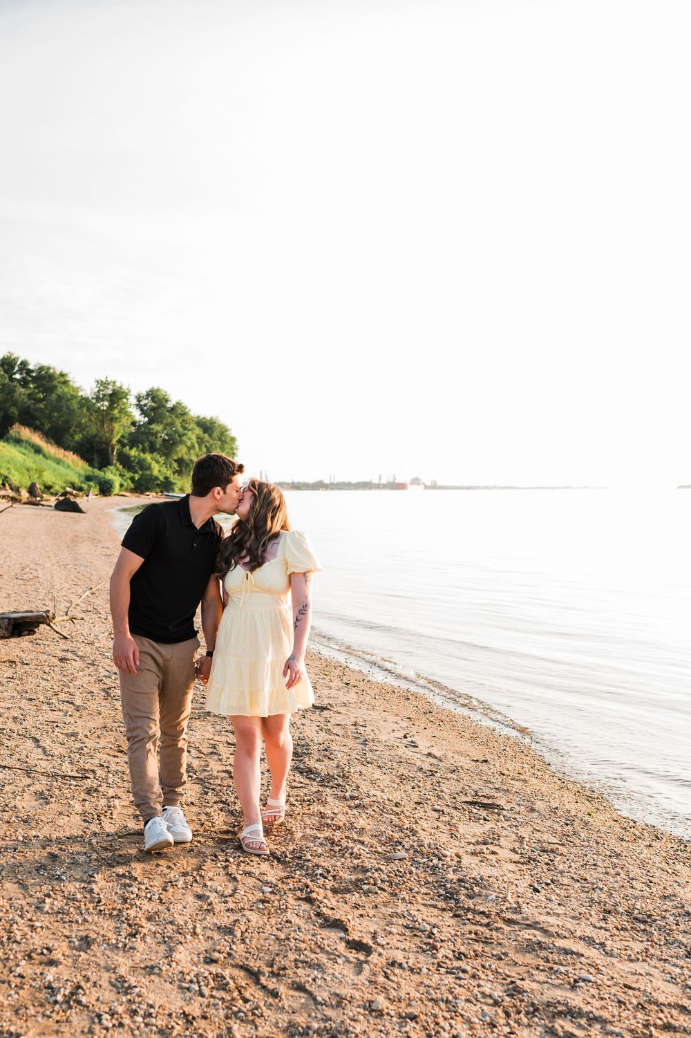A couple walks together on a rocky beach shoreline during golden hour sunset.