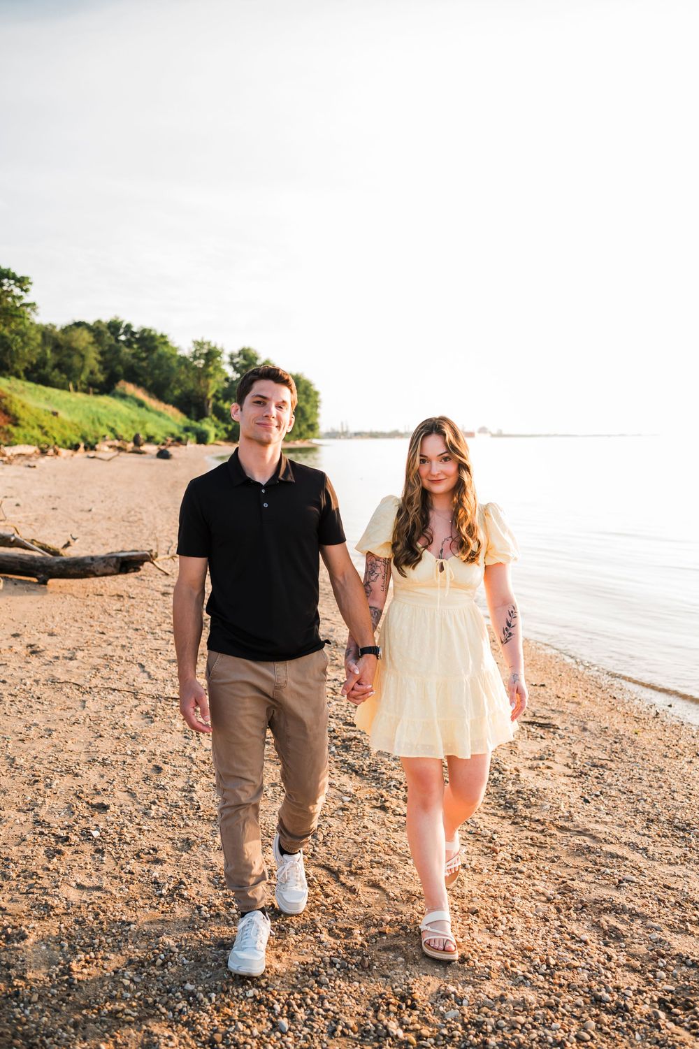 A couple strolls hand in hand along a rocky beach shoreline at sunset.