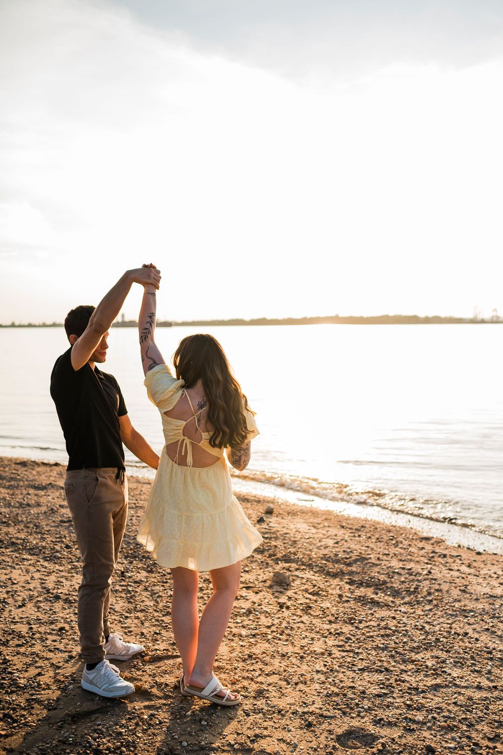 A couple walks along a rocky beach at sunset holding hands and enjoying the peaceful coastal scenery.