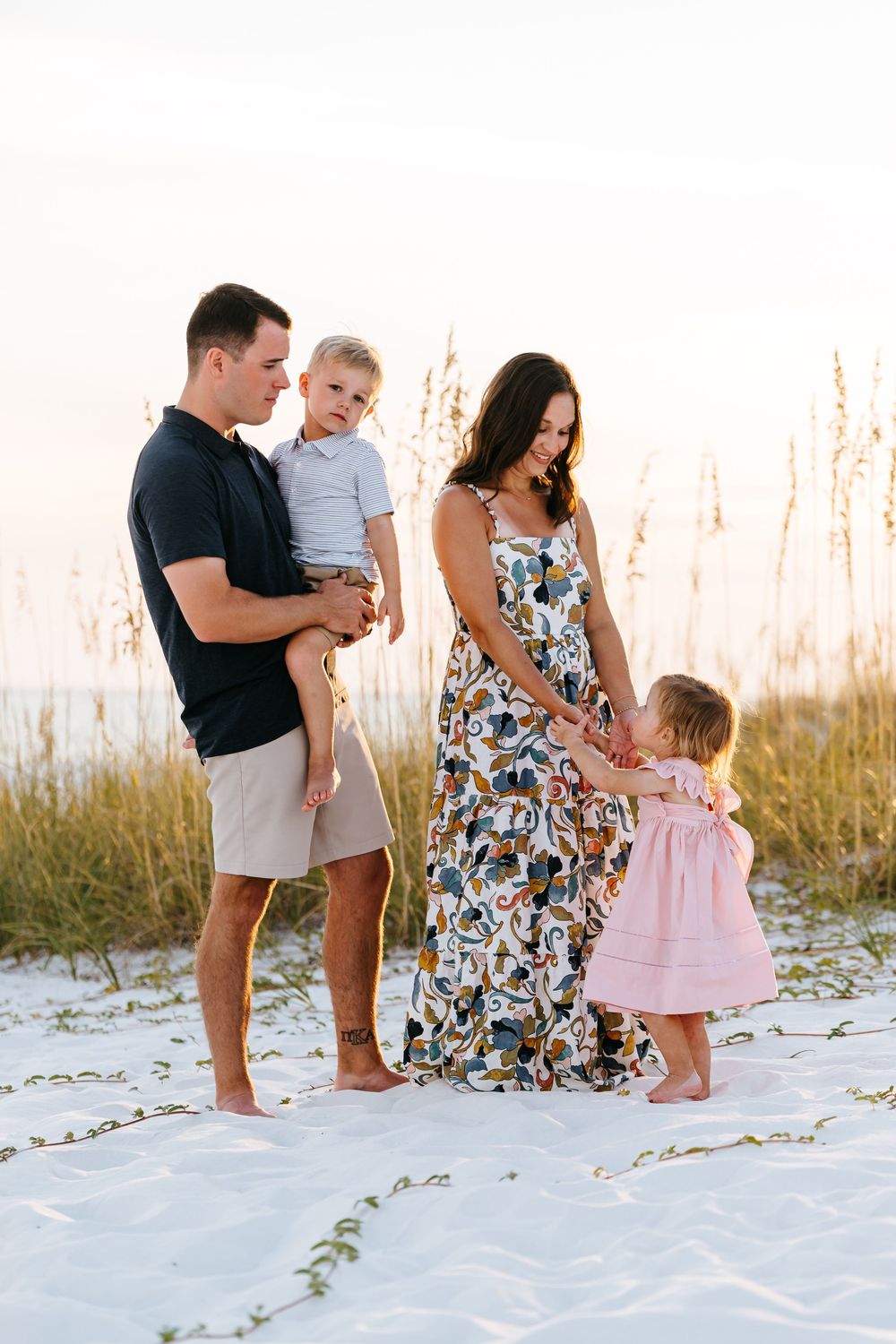Family enjoying time together on white sand beach with sea oats in background.