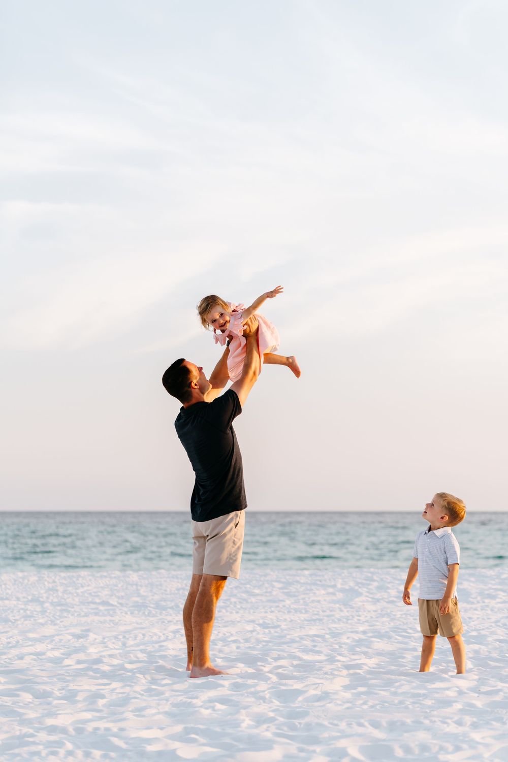 A joyful family moment on a white sandy beach with the ocean in the background during sunset.