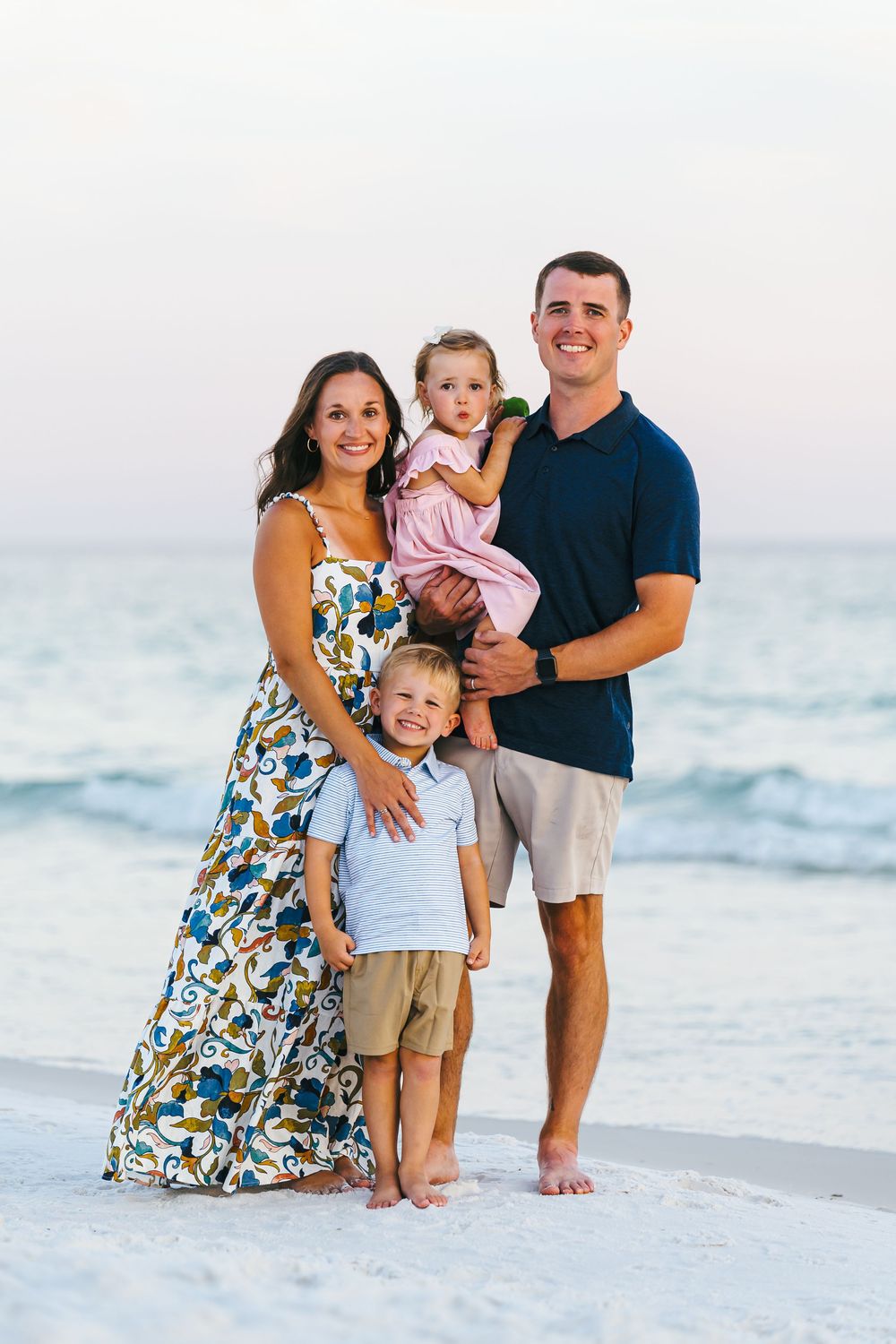 Happy family portrait on beach with ocean waves and sunset in background.