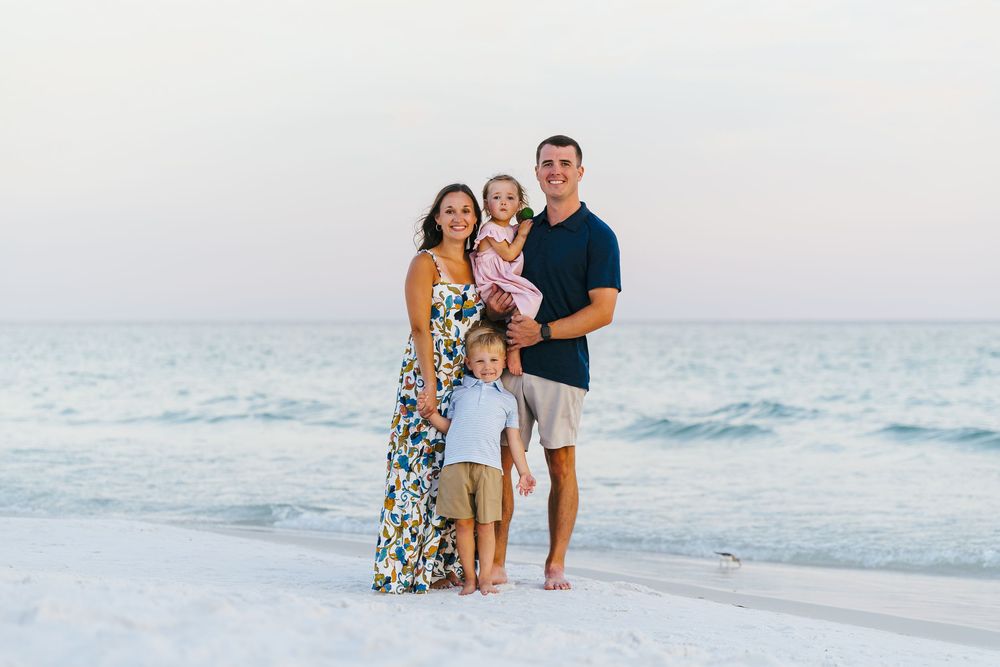 A happy family of four poses together on a pristine white sand beach with the ocean behind them.
