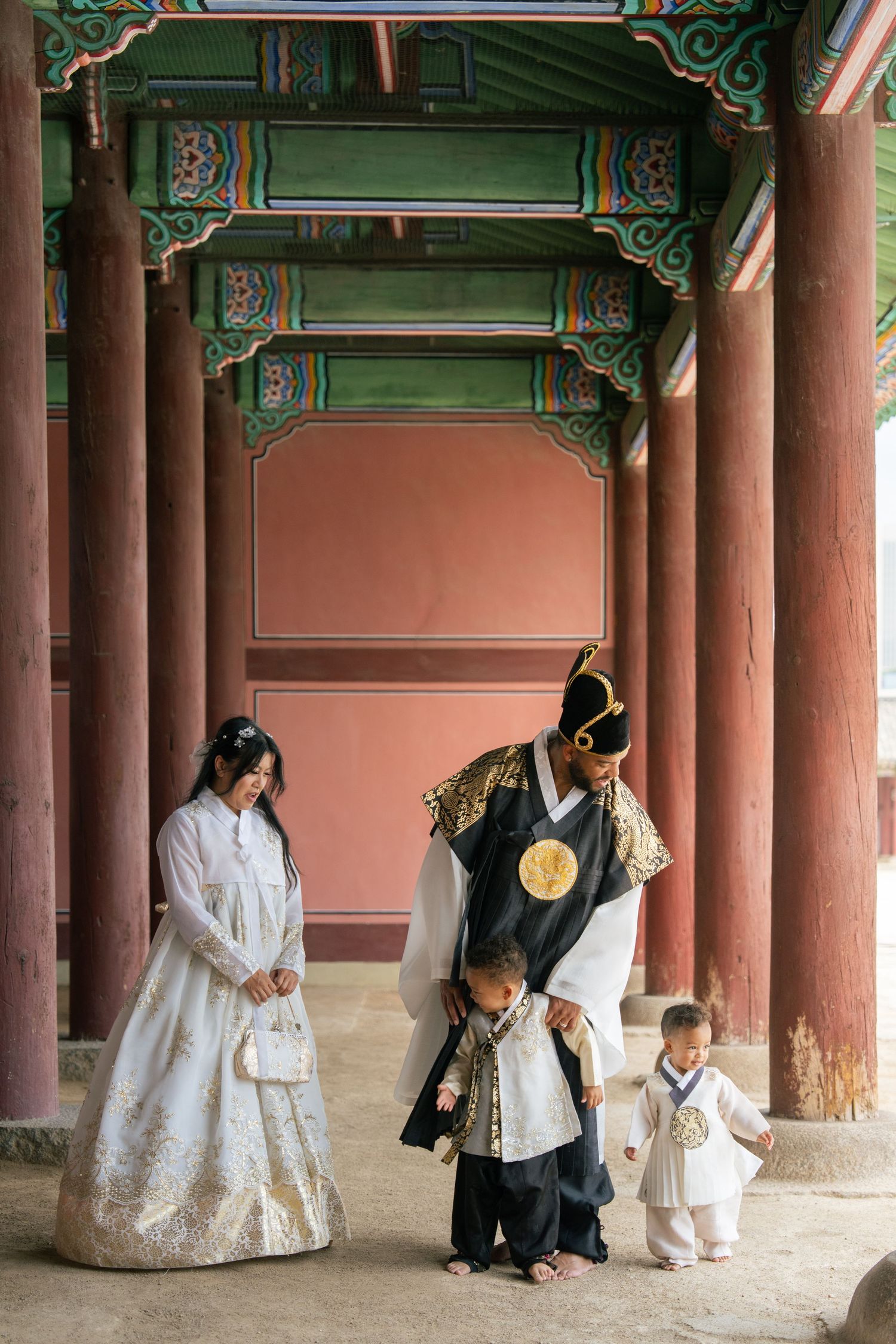 People in traditional Korean hanbok clothing gather under ornate wooden pillars at Gyeongbokgung Palace in Seoul.