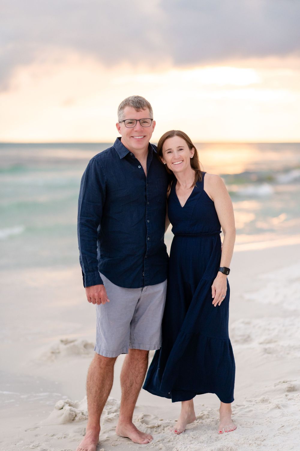 Couple posing together on white sandy beach at sunset in matching navy outfits.
