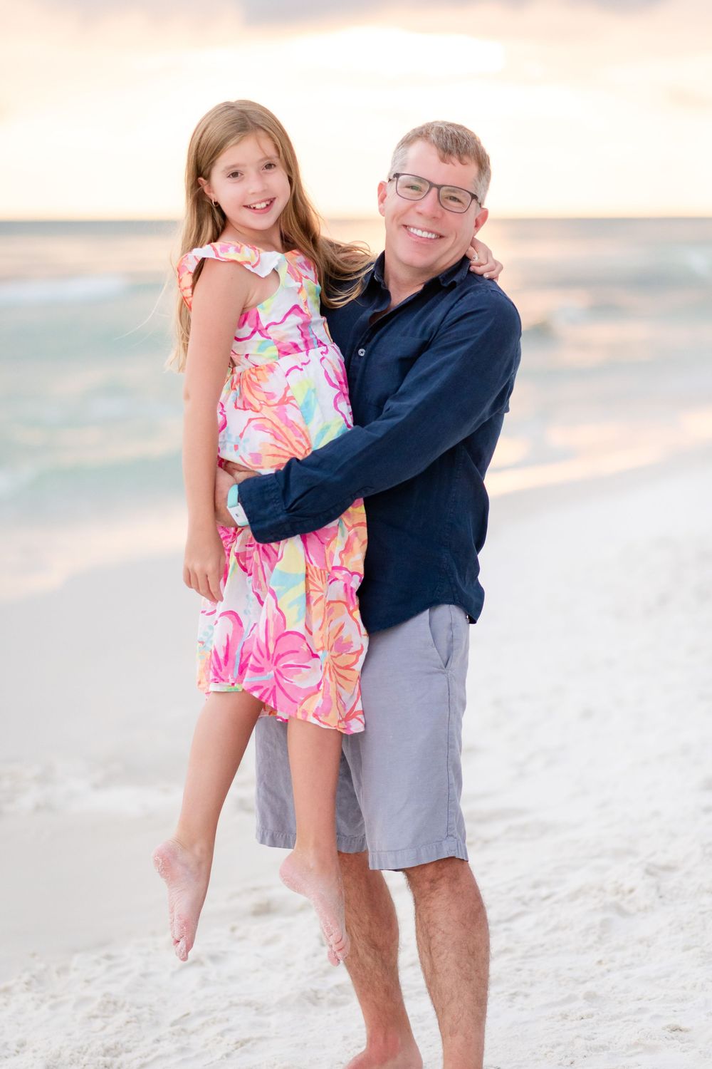 Family portrait on white sandy beach with person in navy sweater and child in pink floral dress.