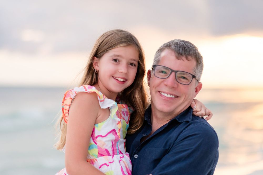 Family members share tender moments together on a beach during golden hour sunset.