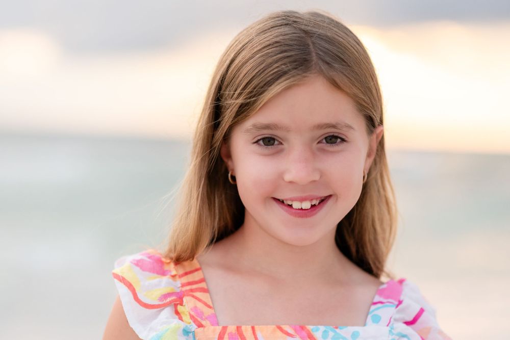 A portrait of a young child wearing a colorful ruffled dress against a soft beach sunset background.