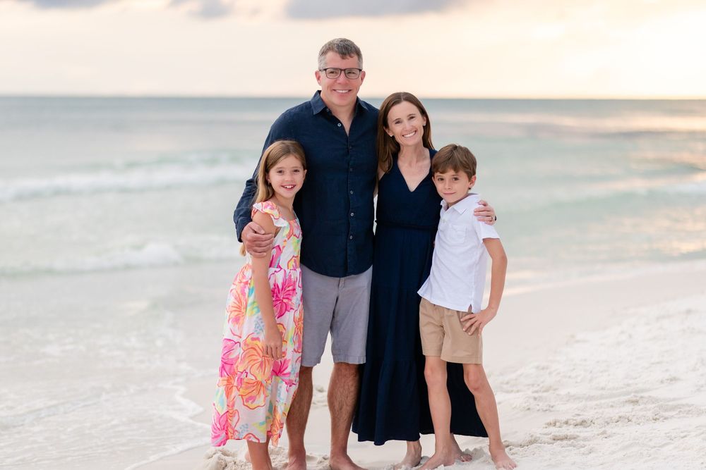 Family enjoying a sunset beach photoshoot with soft pastel colors in the background.