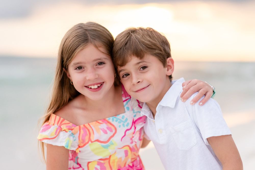 Two children in beach attire smile and pose together during a sunset photo session.