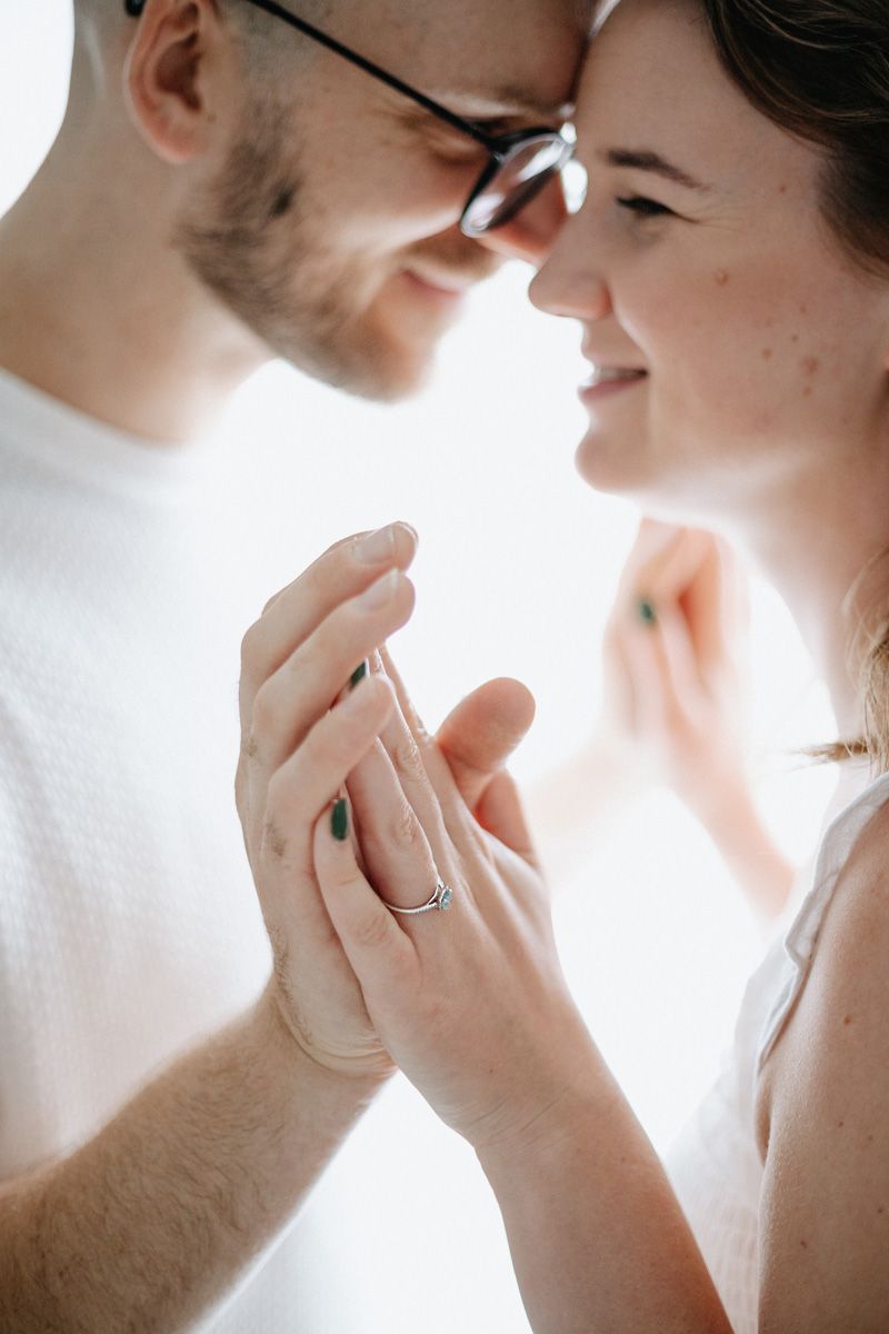 A tender romantic moment between a couple holding hands with a sparkling engagement ring visible.