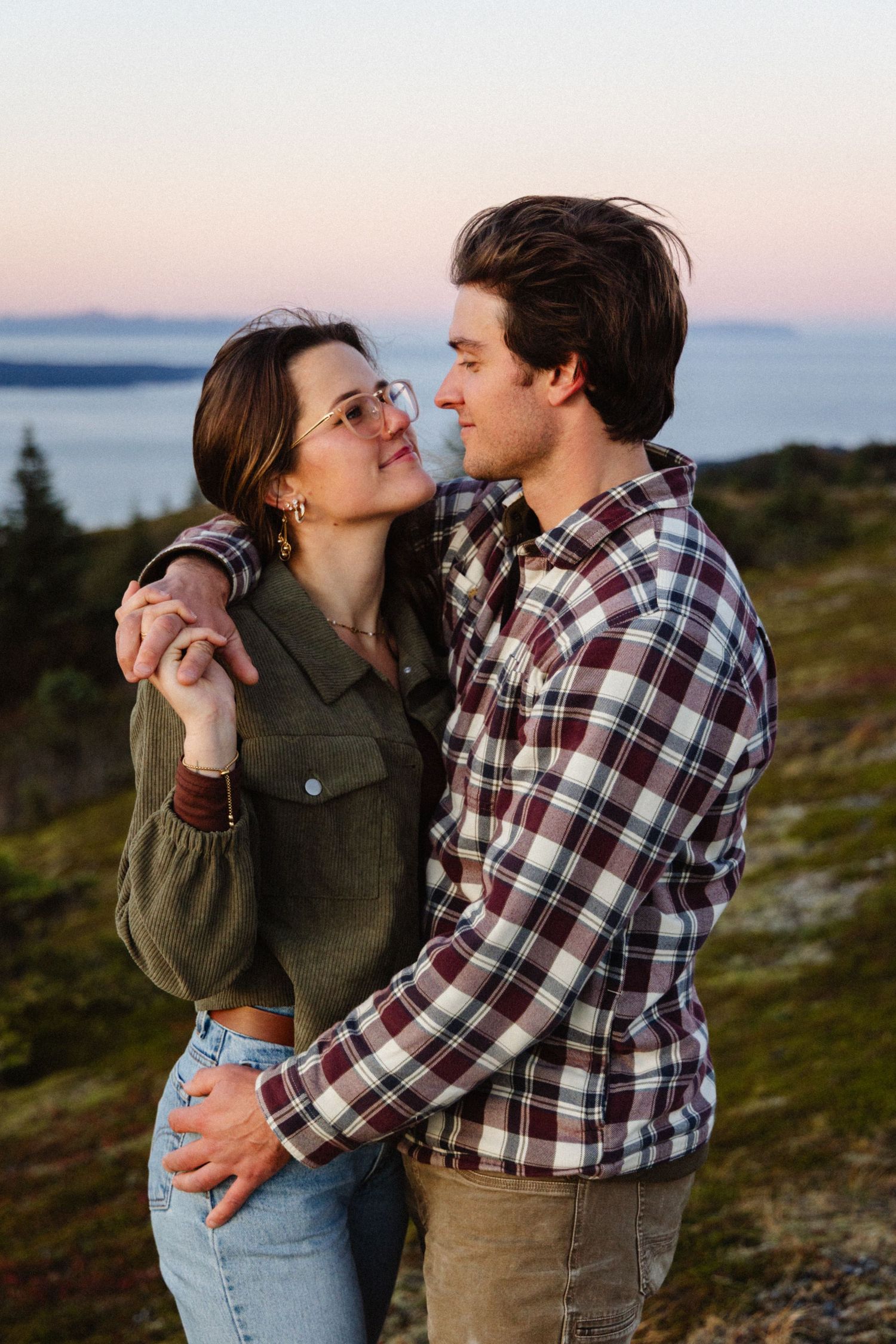 A romantic proposal unfolds along a scenic coastal cliff with mountains and ocean views at golden hour.