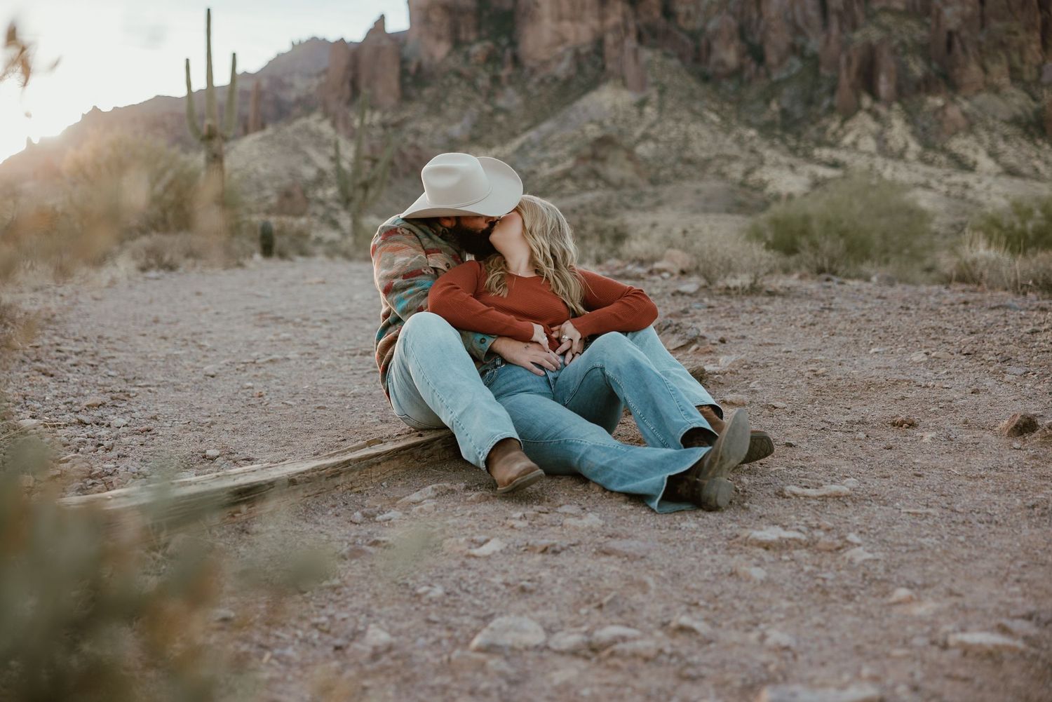 Couple sitting together in a desert landscape during sunset, creating a romantic silhouette against the rocky terrain at Lost Dutchman.