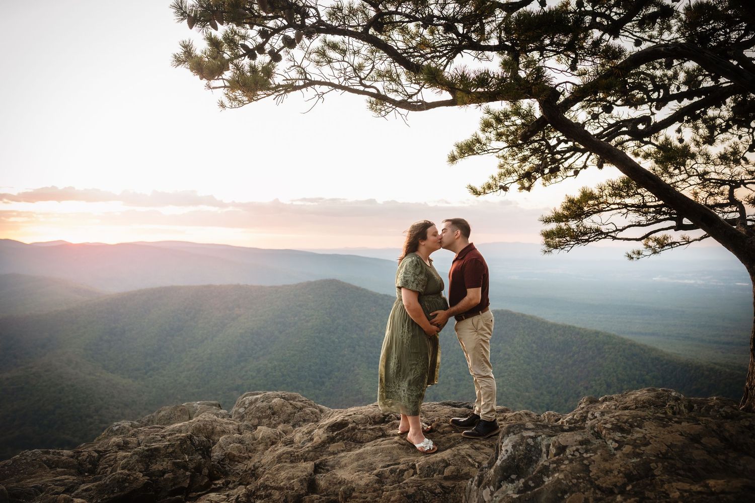 Expectant parents kiss in the breeze on Raven's Roost Overlook at golden hour, captured by Charlottesville newborn photographer.