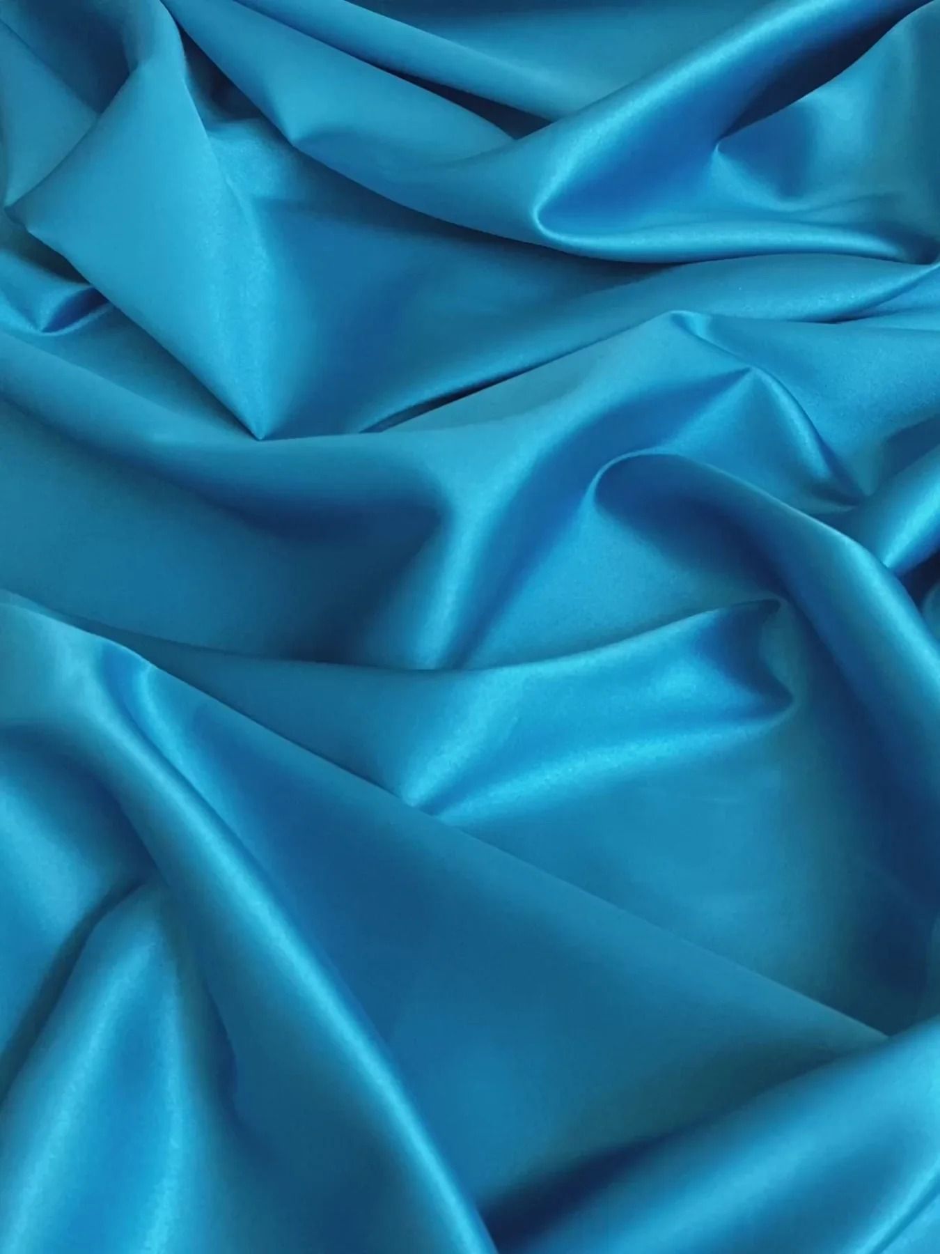 Silky turquoise fabric with soft folds creates a luxurious texture and sheen in close-up detail.