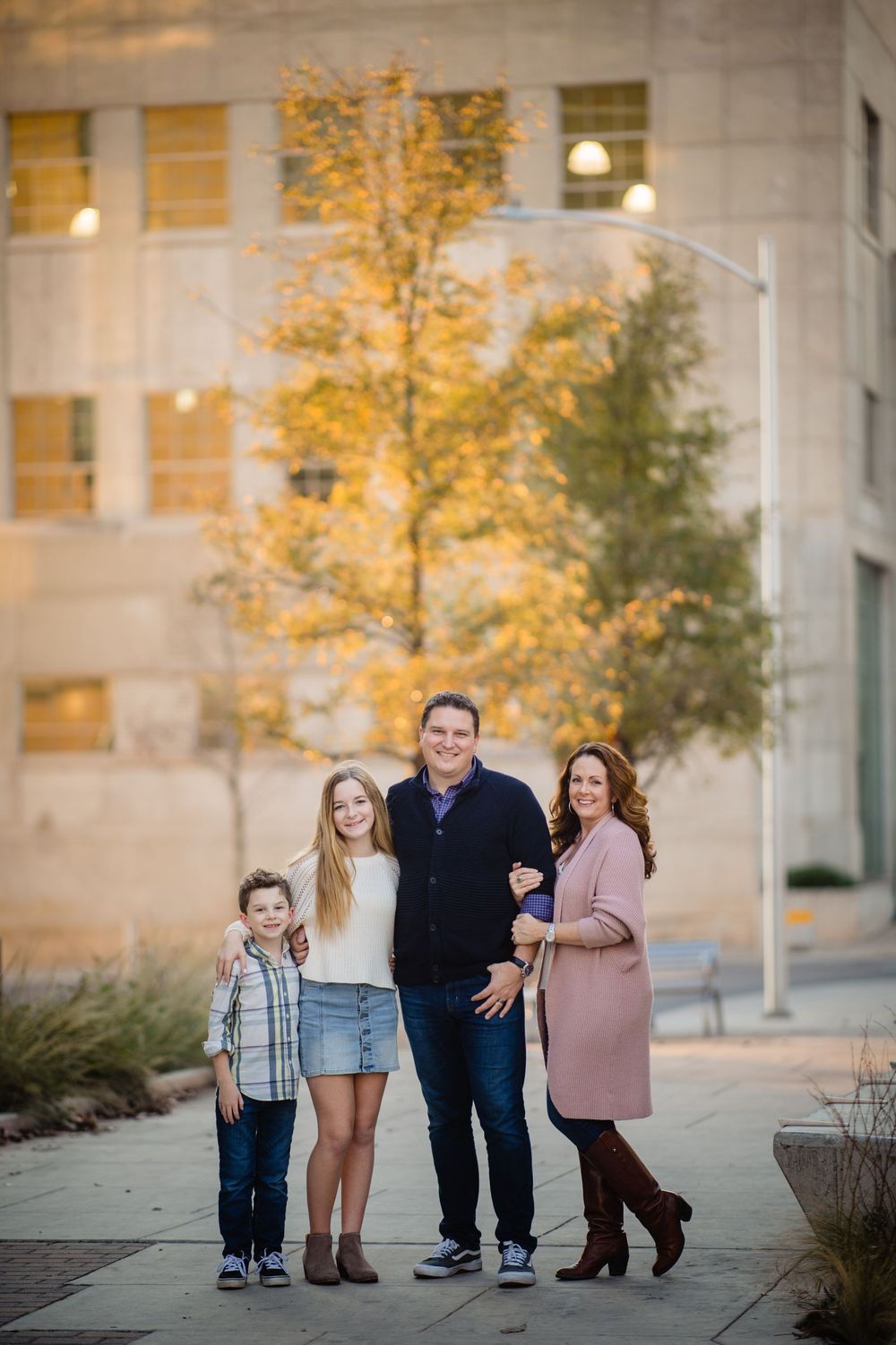 A group stands together on an urban sidewalk in autumn with yellow trees and a building facade in the background.