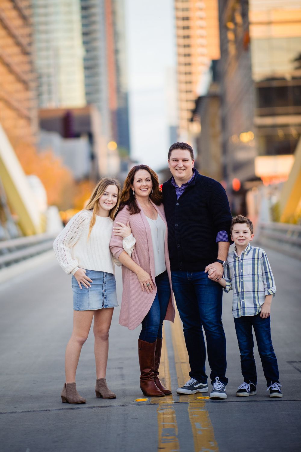 A family poses together on an urban bridge at sunset with city buildings visible in the background.