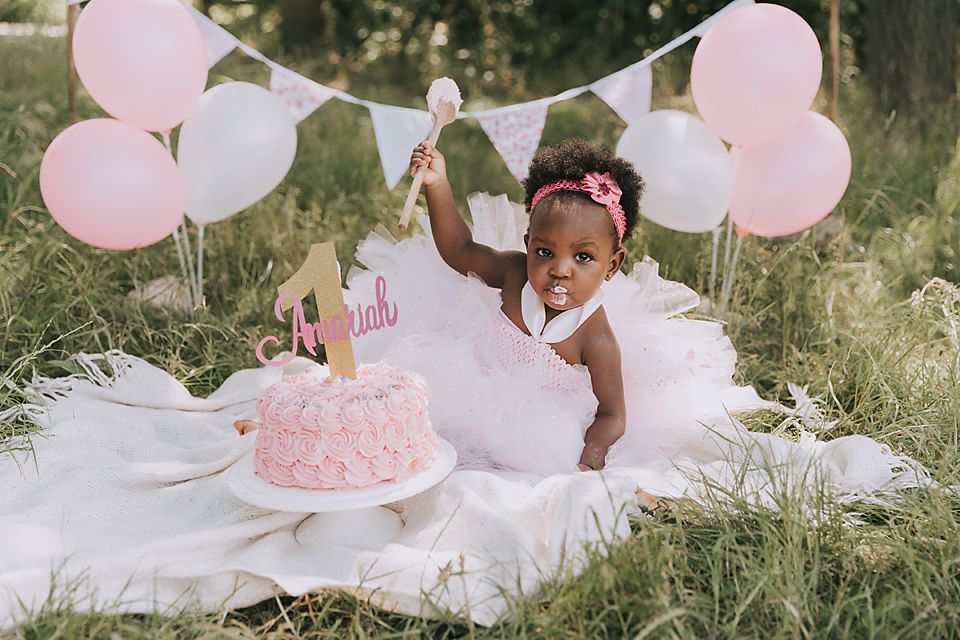 Pink and white themed first birthday photoshoot setup in natural outdoor setting.
