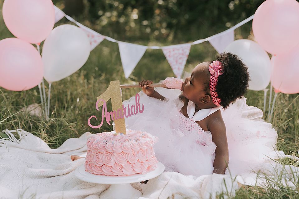 Pink and white themed cake smash photoshoot setup in outdoor garden setting with balloons and decorative bunting.