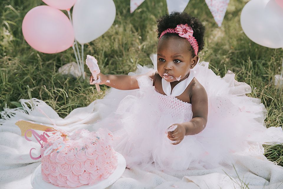 Festive outdoor cake smash photography session with pink and white party decorations.