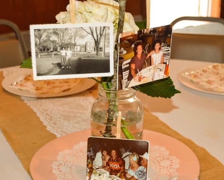 Vintage photographs displayed in small glass vases on pink doily placemats at a table setting.