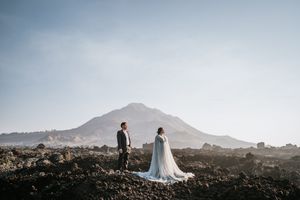 Two figures in wedding attire stand together against a dramatic mountain landscape at sunset.