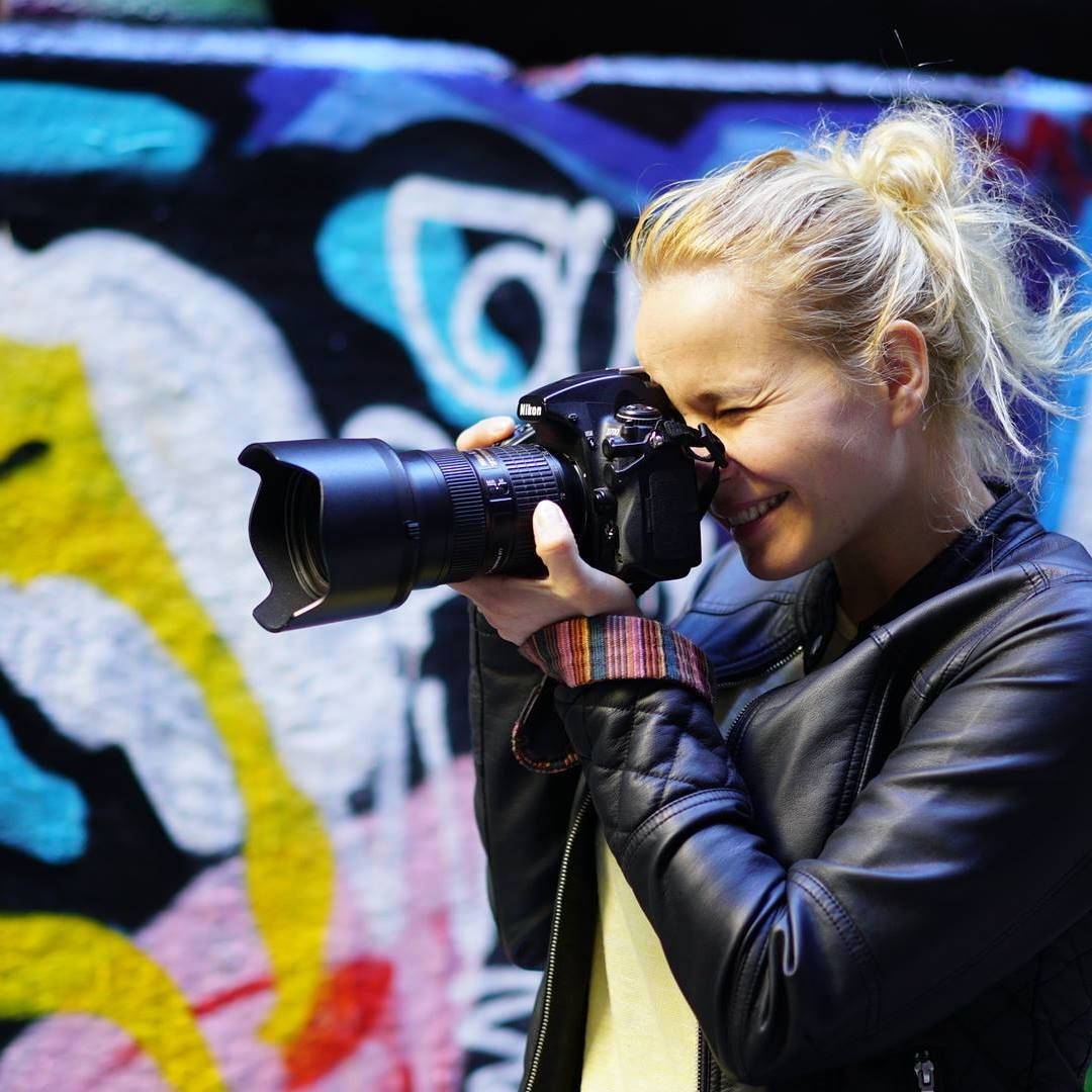 A photographer in a leather jacket takes pictures against a colorful graffiti wall backdrop.