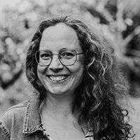 Frau mit lockigem langen Haar un Brille lacht in die Kamera. Schwarz-Weiss Fotografie.