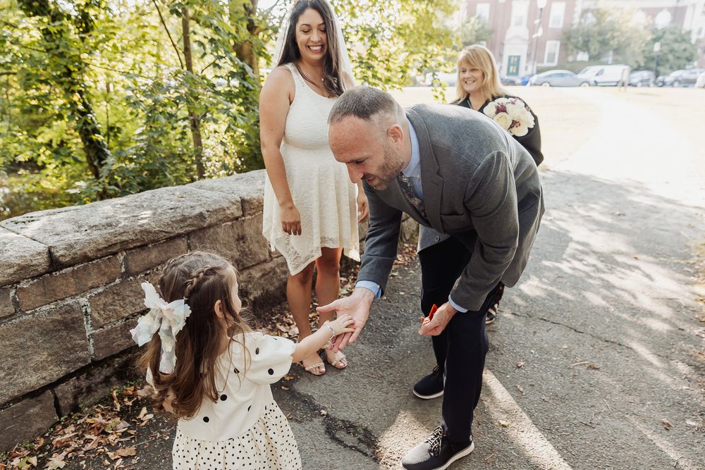 A family shares a tender moment together on a sunny path bordered by stone walls and greenery.