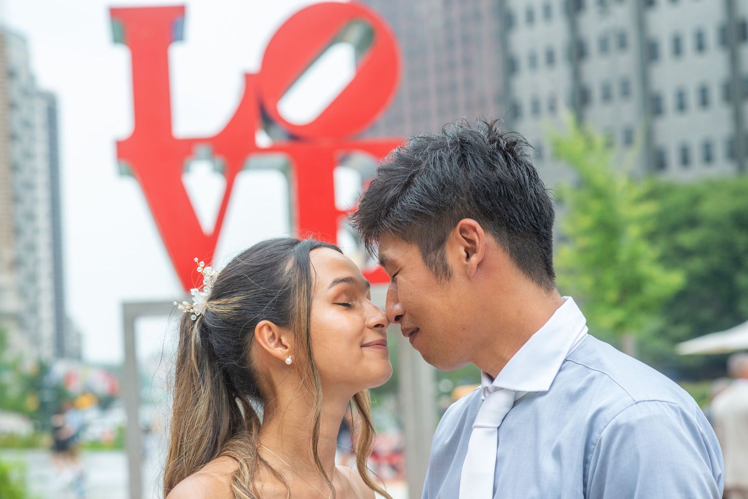 A couple in wedding attire shares a romantic moment in front of an urban backdrop with red letters.