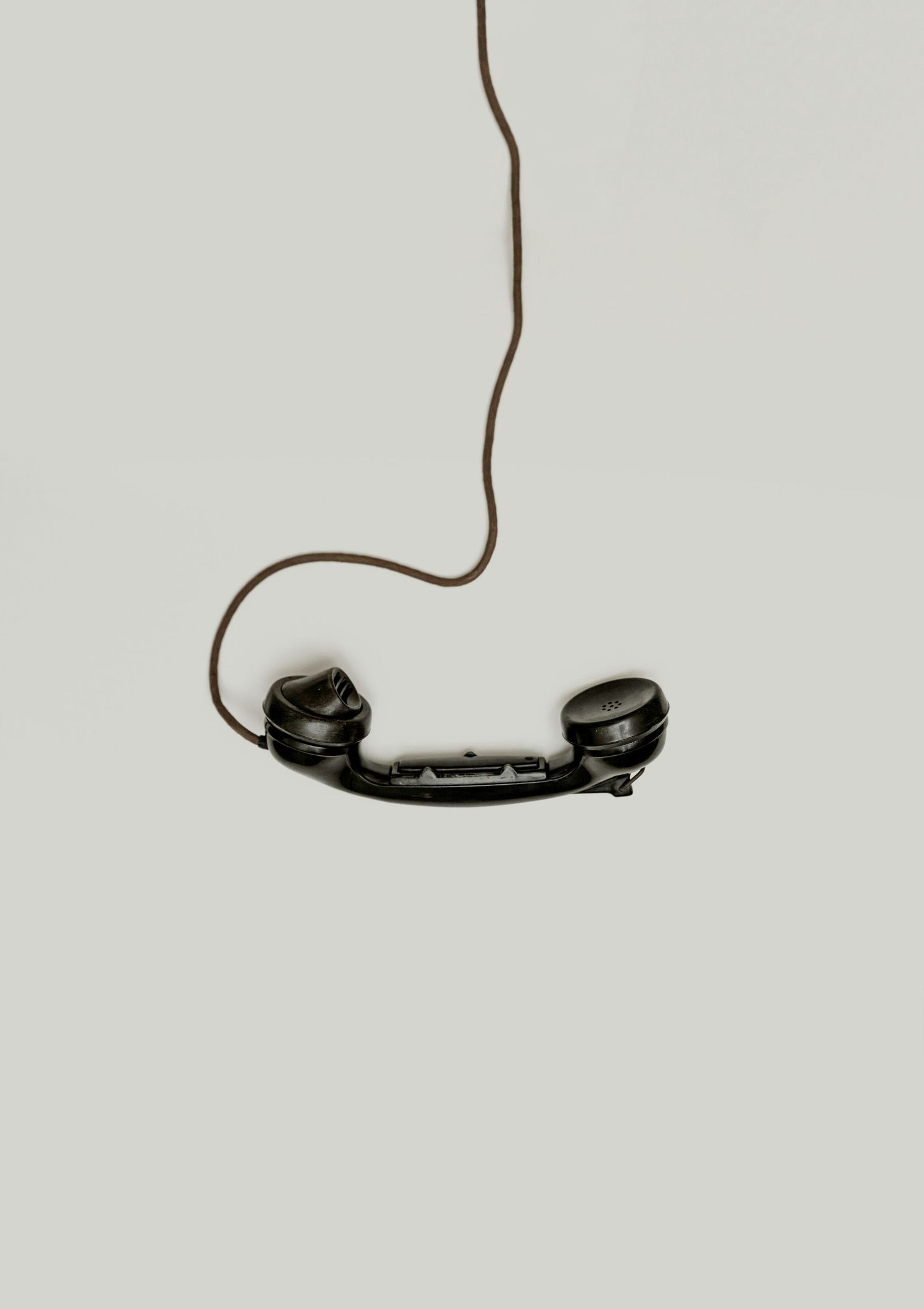 Image minimaliste en noir et blanc d’un combiné téléphonique vintage suspendu par son cordon.