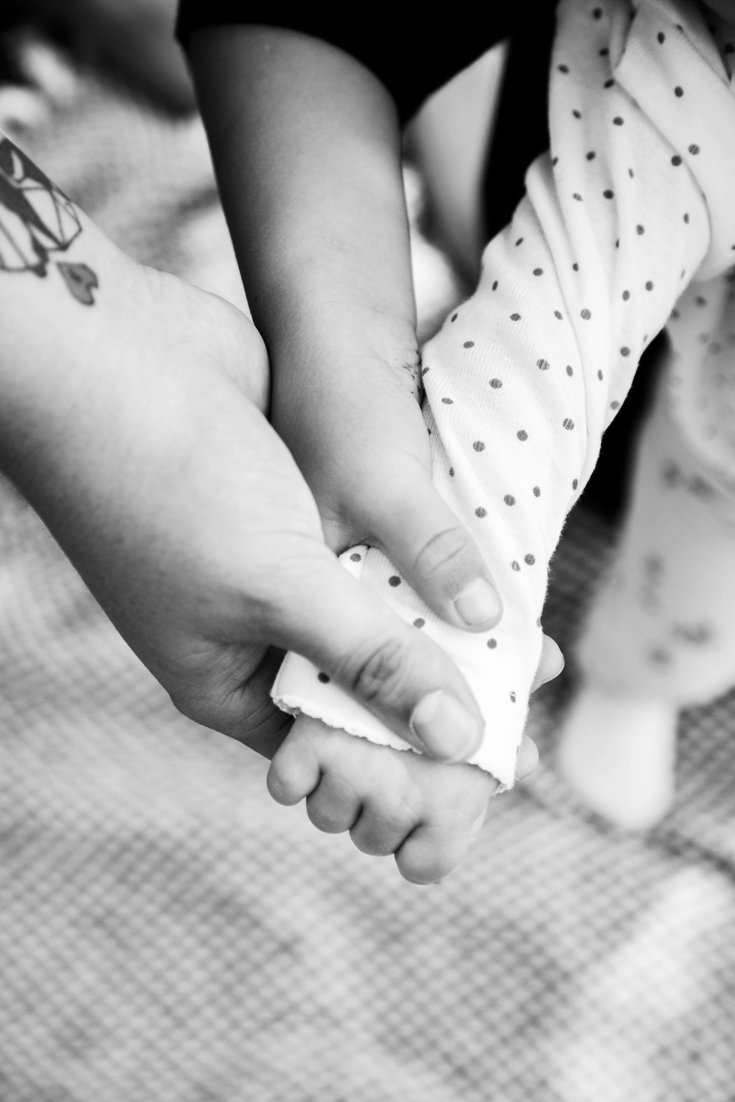 a Childs arm with another child and their mom also holding their hand